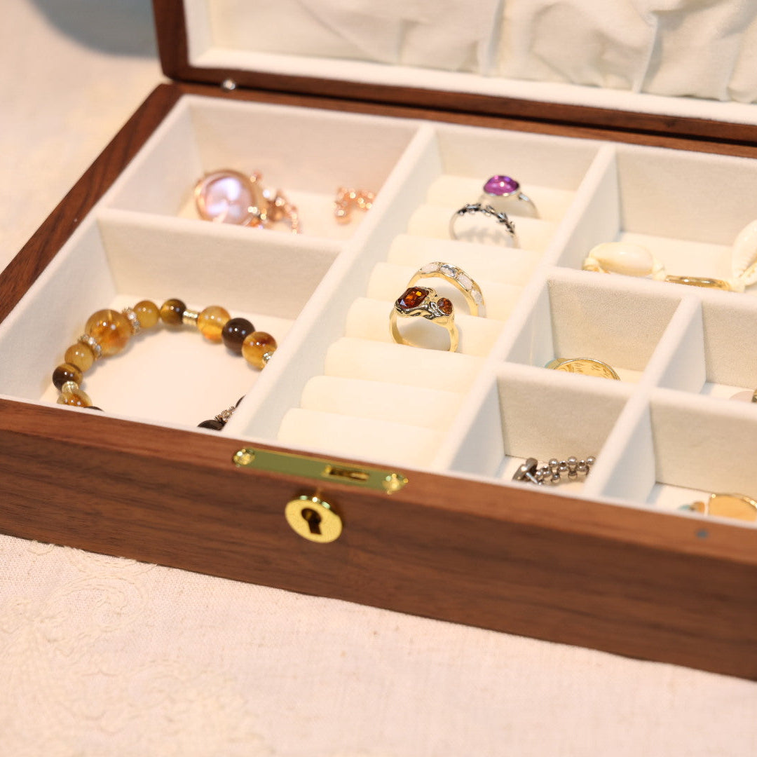 Wooden jewelry box with compartments containing jewelry items on a light background