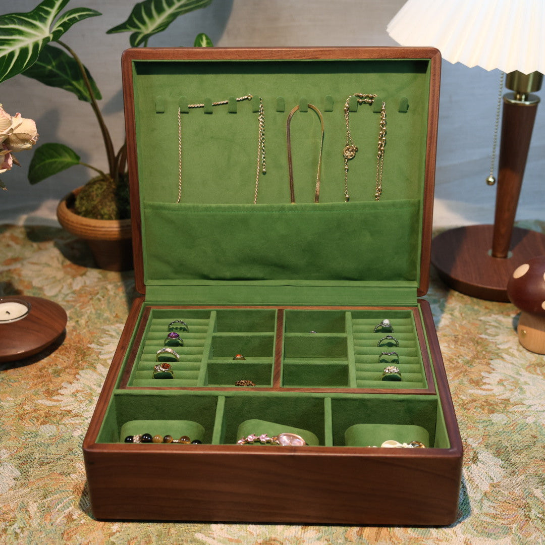 Jewelry box with green interior containing necklaces and earrings on a patterned tablecloth.
